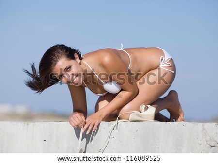 Girl at the sea. Young woman in white swimwear on all fours looking at camera smiling on open air