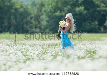 Young woman with bouquet of flowers walking through chamomile field