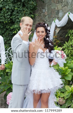 Newly wedded couple in the park. Just married are showing middle fingers with wedding rings in day of them wedding
