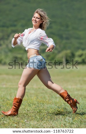 Ukrainian girl in field. Attractive blond woman in blouse with ukrainian embroidery running along field. Vertical composition