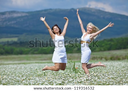 Attractive young women jumping in chamomile field with raised hands. Jumping girls