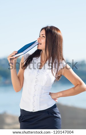 Attractive long haired brunette on open air. Young business woman biting notebook