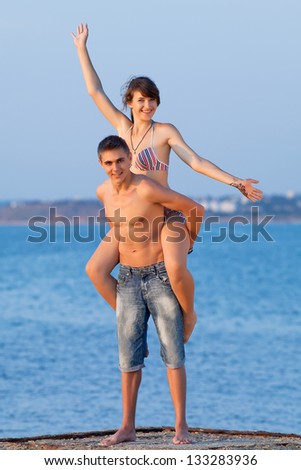 Piggyback. Attractive guy and girl are playing at the sea in evening time