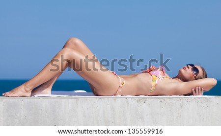 Young woman in bikini at the sea. Attractive woman in swimwear lying on concrete pier looking up