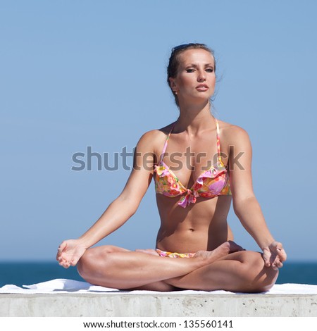 Young woman in bikini at the sea. Attractive woman in swimwear doing yoga at the sea