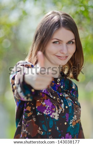 Portrait of attractive young woman on open air. Business woman making a thumb up sign outdoors