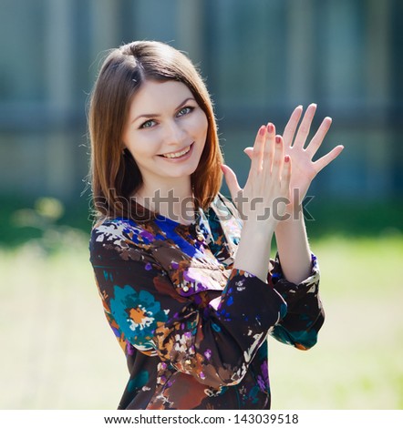 Attractive brunette in blouse outdoors. Young business woman claps and looks at camera on open air