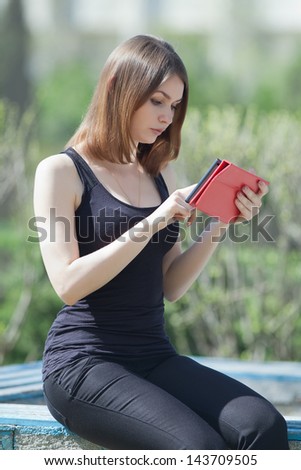 Attractive young woman in the park. Girl uses touchpad on open air