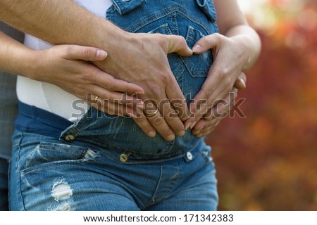 Four hands on belly of expectant mother. Couple posing a heart with their fingers on belly of expectant mother