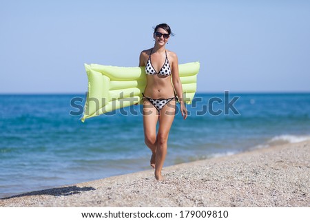 Girl at the sea. Young woman with swimming mattress walking along the sea looking at camera