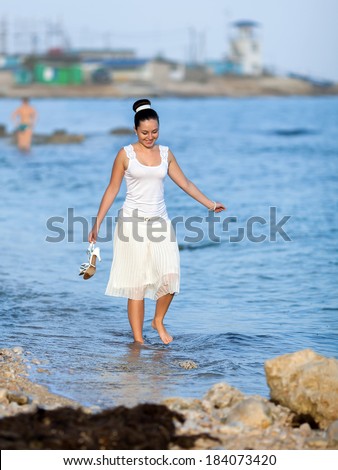 Girl on seashore. Barefoot girl with shoe in her hands walks on water