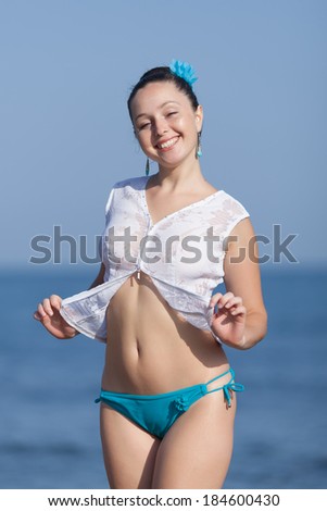 Girl at the sea. Young woman in white blouse and blue swimming trunks posing on background of sea looking at camera smiling