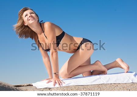 Attractive young woman in black swimsuit on all fours on background of the sky