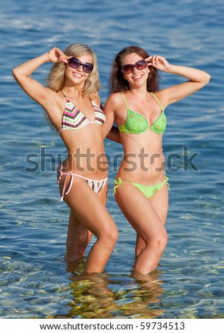 Two attractive girls in bikini smiling and looking through sunglasses at camera