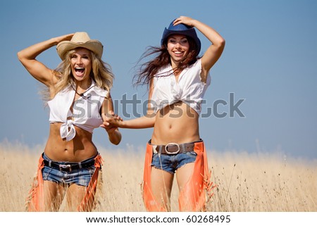 Two girls are walking at the field. Young women in costumes of cowboys outdoors
