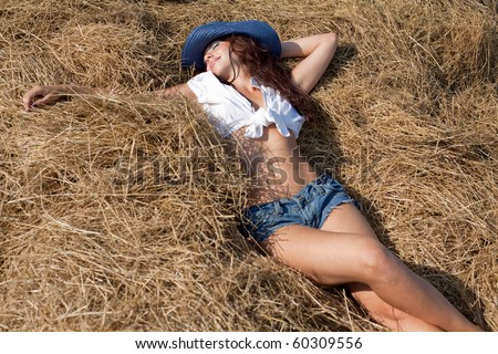 Portrait of brunette girl in shorts and hat. Young woman in costume of cowboy lies on haystack