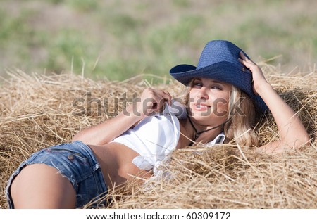 Portrait of blond girl in hat. Young woman in costume of cowboy lies on haystack