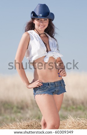 Portrait of brunette in hat at the field. Young woman in costume of cowboy looks at camera