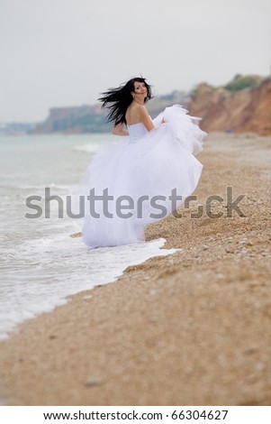 Girl in wedding dress running along the beach