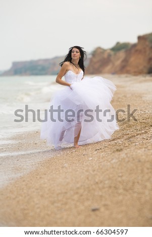 Girl in wedding dress running along the beach