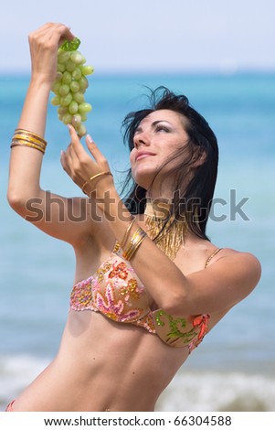 Brunette in costume for oriental dancing with grape on the beach
