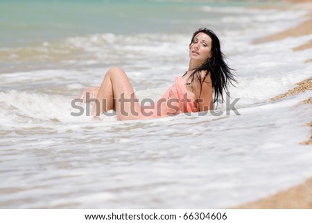 Attractive brunette in a pink pareo sits in the surf line
