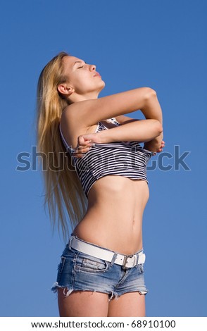 Undressing girl in shorts outdoors. Attractive young woman undresses on background of clear sky