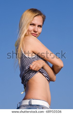 Pretty blond undressing looking at camera. Attractive young woman undresses on background of clear sky