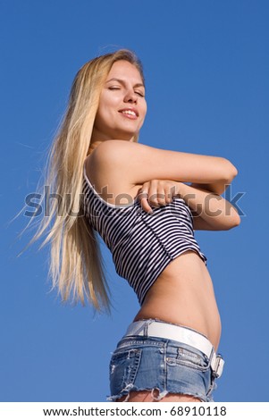 Undressing girl in shorts outdoors. Attractive young woman undresses on background of clear sky