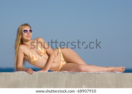 Blonde in bikini and sunglasses at the sea. Attractive young woman in bikini looks at camera through sunglasses smiling