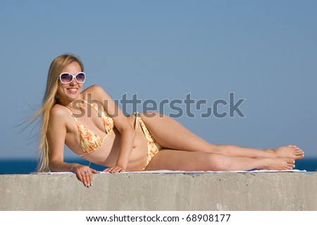 Blonde in bikini and sunglasses at the sea. Attractive young woman in bikini looks at camera through sunglasses smiling