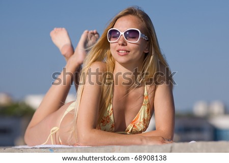 Blonde in bikini and sunglasses at the sea. Attractive young woman in bikini lies on the beach