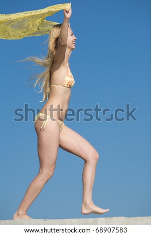 Attractive blond girl in bikini on the beach. Young long-haired blond woman in bikini with yellow pareo is running along the coast