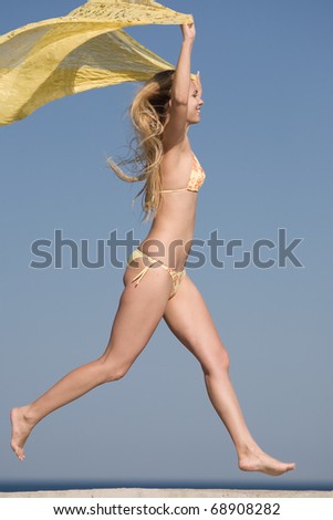 Attractive blond girl in bikini on the beach. Young long-haired blond woman in bikini with yellow pareo is running along the coast
