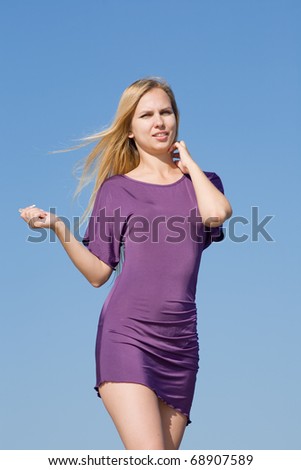 Attractive young woman in violet dress outdoors. Blonde in violet dress looking at camera