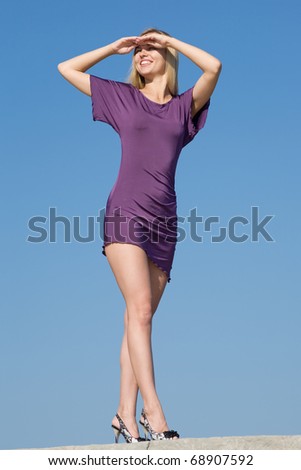 Blonde in violet dress on background of the sky. Attractive young woman in violet dress outdoors