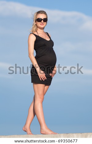 Pregnant woman in black dress outdoors. Expectant mother on background of the sky