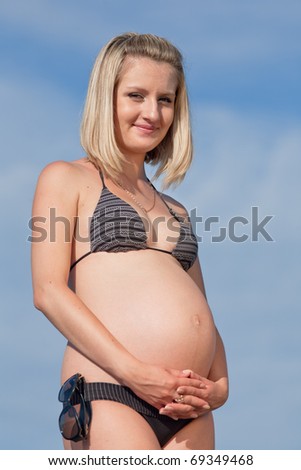 Pregnant woman in swimwear outdoors. Attractive expectant mother in bikini looks at camera smiling