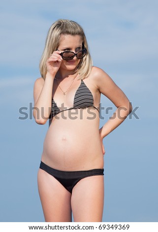 Pregnant woman in swimwear outdoors. Attractive expectant mother in bikini looking on top of sunglasses at camera