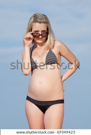 Pregnant woman in swimwear outdoors. Attractive expectant mother in bikini looking on top of sunglasses at camera