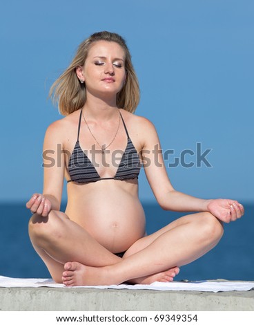 Pregnant woman in swimwear outdoors. Attractive expectant mother in bikini sits on background of sea