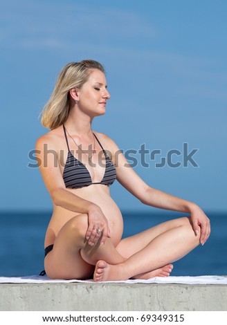 Pregnant woman in swimwear outdoors. Attractive expectant mother in bikini sits on background of sea