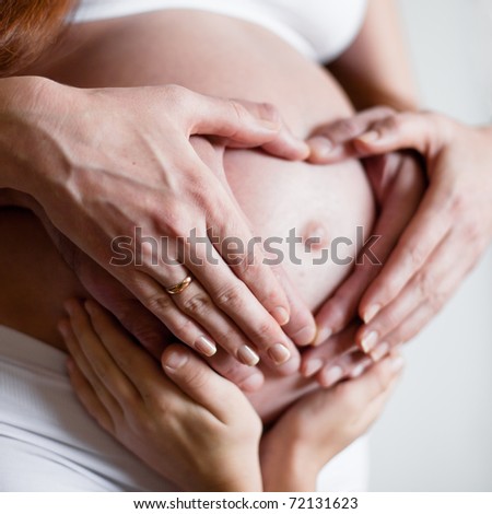 Six hands on belly of expectant mother. Family posing a heart with their fingers on belly of expectant mother