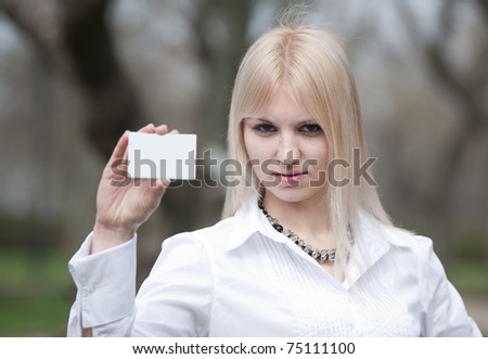 Attractive young woman in the park. Blonde in white is showing plastic card outdoors
