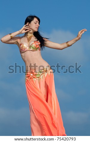 Brunette in costume for belly-dance is dancing on background of sky. Girl is dancing outdoors
