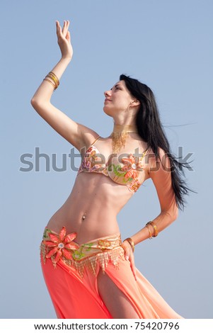 Brunette in costume for belly-dance is dancing on background of sky. Girl is dancing outdoors