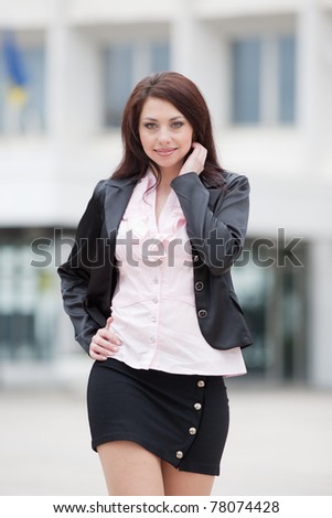 Attractive business woman on background of building. Cute business woman walking outside on a grey day