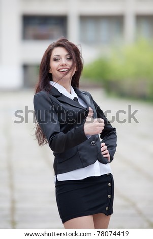 Attractive business woman on background of building. Cute business woman showing thumb up smiling