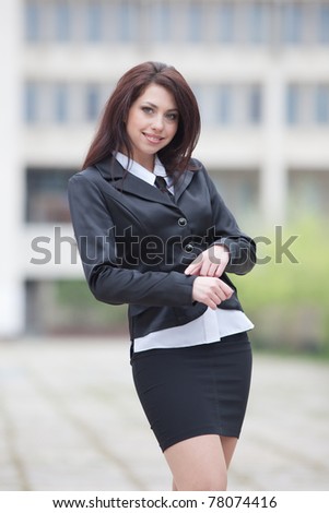 Attractive business woman on background of building. Cute business woman checking time looking at camera