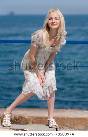 Slim blonde on seashore. Attractive young woman holds her skirt blown by wind